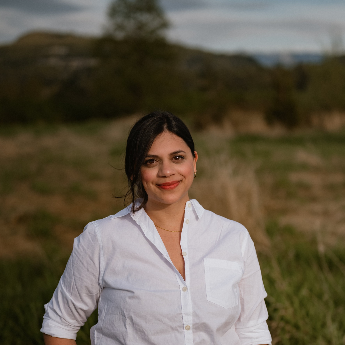 Woman in a white shirt and green pants standing in a grassy field.