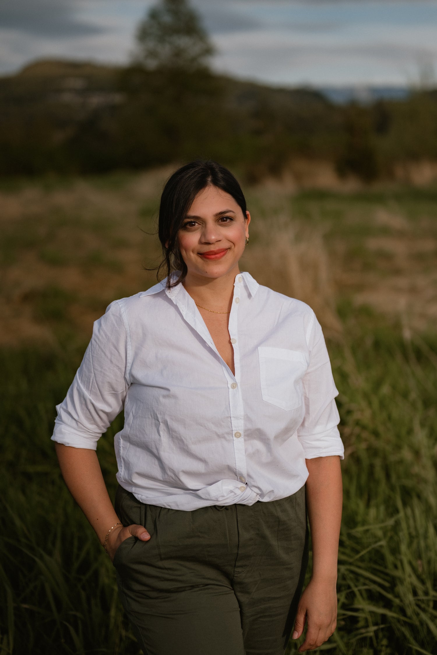 Woman in a white shirt and green pants standing in a grassy field.