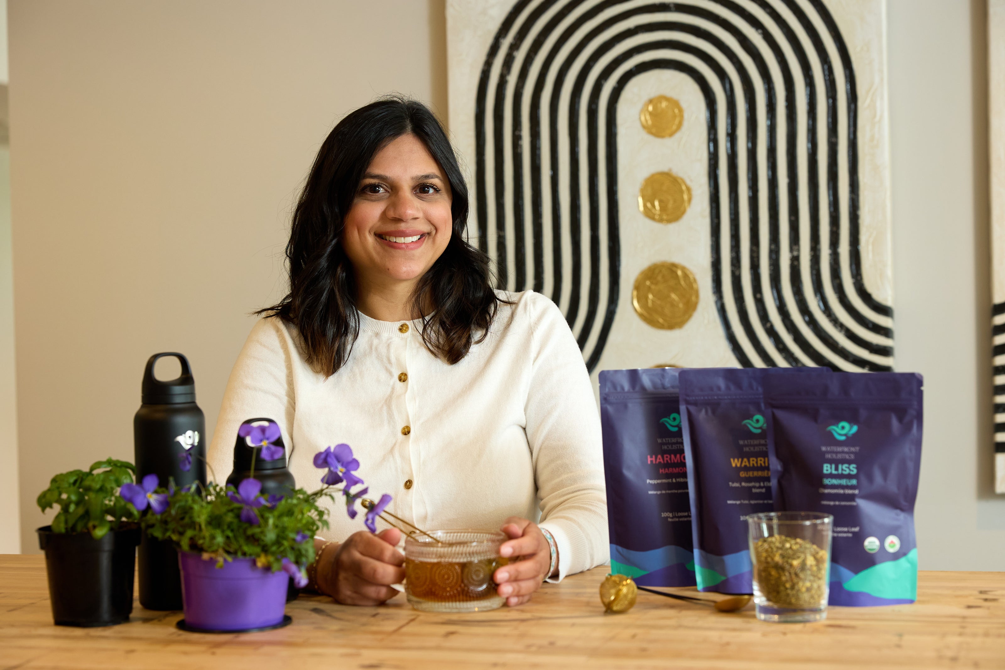 Woman sitting at a table with tea and packaging, with decorative elements in the background