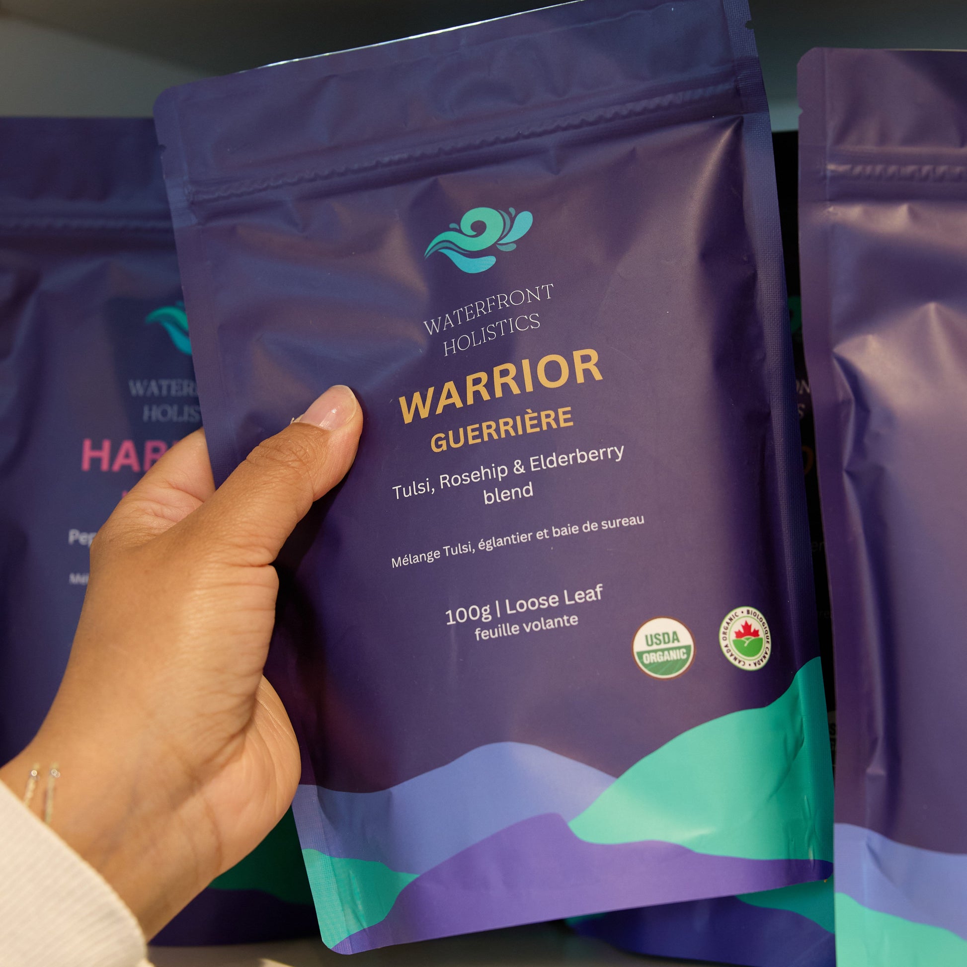 Hand holding a purple 'Warrior' supplement package on a shelf with other similar packages.