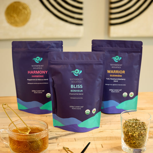 Three packages of 'Harmony', 'Bliss', and 'Warrior' on a wooden surface with tea-making tools.